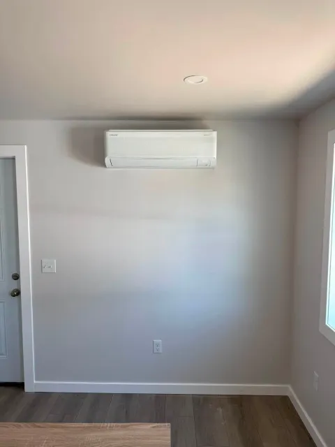 Small empty room with gray walls, wall-mounted AC unit, and a window on the right.
