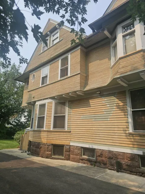 Before: side of a three-story house with faded yellow siding
