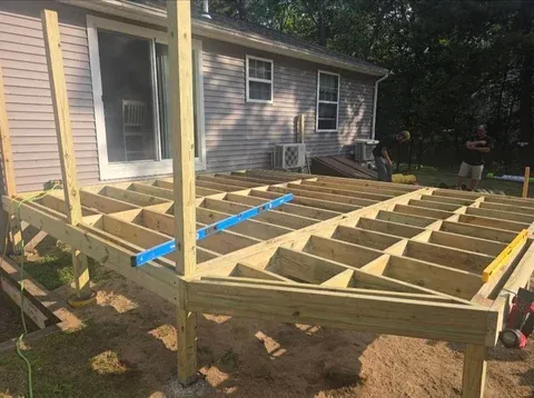 Wooden deck frame under construction with exposed joists and support beams attached to a residential house