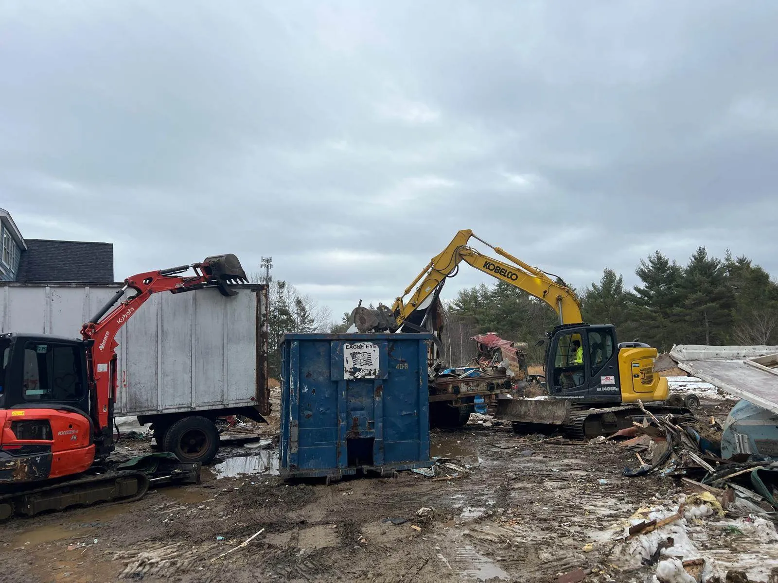 Excavator loading demolition debris into a roll-off dumpster for property cleanup