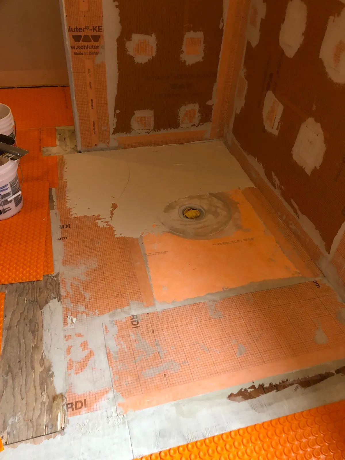 Tiled shower floor and walls mid-renovation, with orange waterproofing membrane and patchy cement board.
