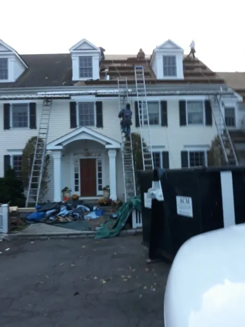 A man on a ladder is working on the roof of a house