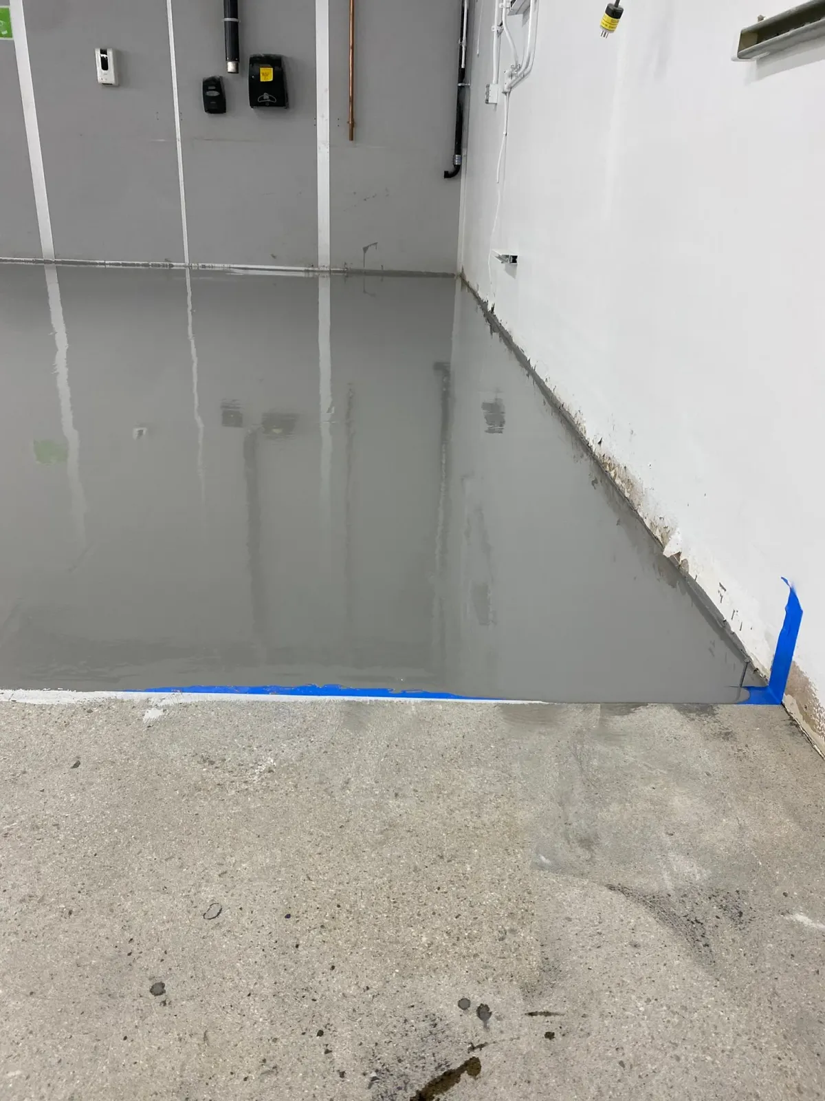 Flooded indoor room with standing gray water beside a dry concrete floor and unfinished walls