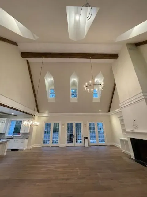Spacious living room with vaulted ceiling, skylights, large windows, hardwood floors, and a chandelier.