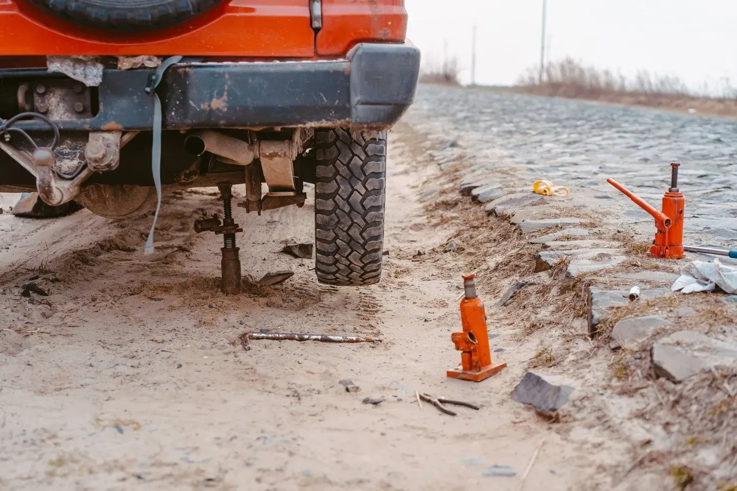 Orange truck on a muddy roadside with small orange survey markers beside a cracked ditch