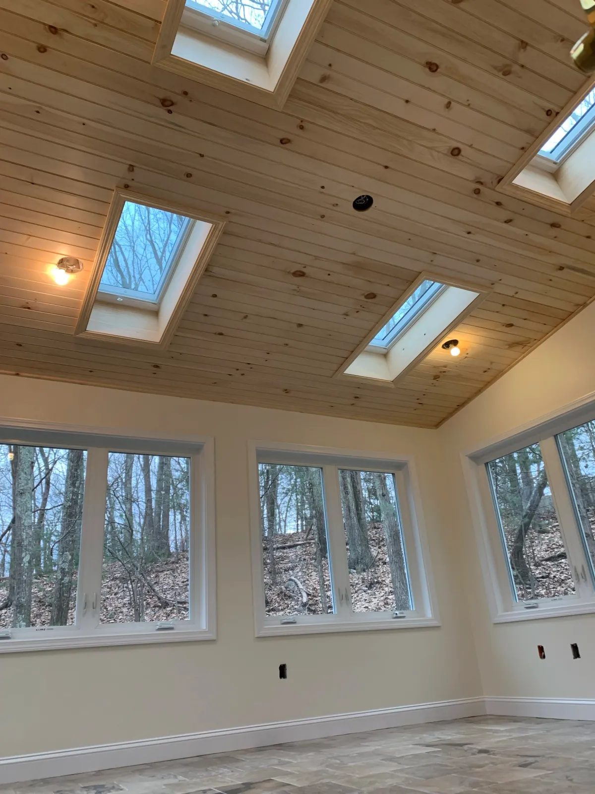 A room with large windows and a wooden ceiling with four skylights; the room appears to be under construction or renovation.