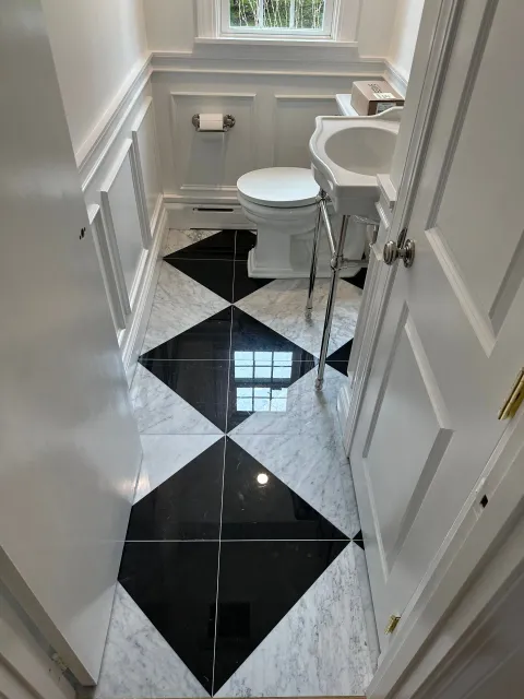 Narrow bathroom with black-and-white diamond tile floor, toilet, sink, and window above.