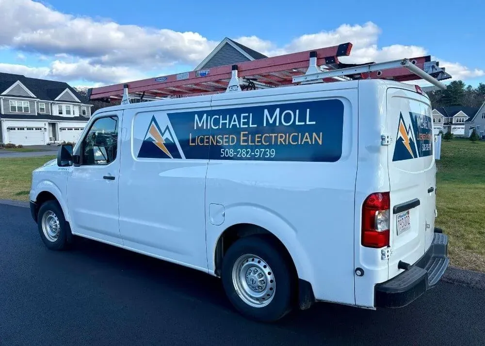The work van for Michael Moll Licensed Electrician in Northbridge, MA is parked in a driveway with the van lettering viable.