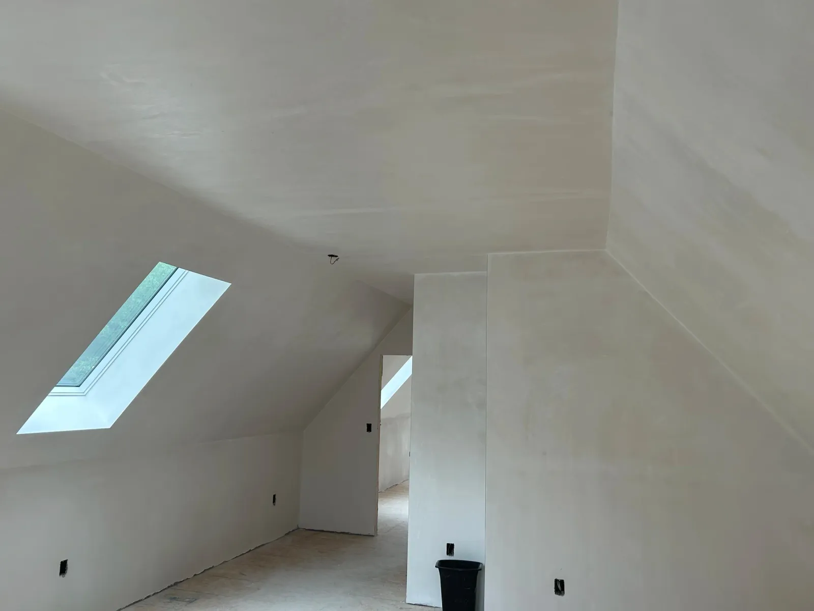 An unfinished room with sloped ceiling and skylight windows, white walls, and electrical outlets.