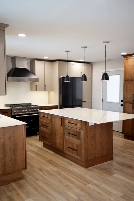 Modern kitchen with wood cabinets, a white countertop island, black appliances, and three black pendant lights.