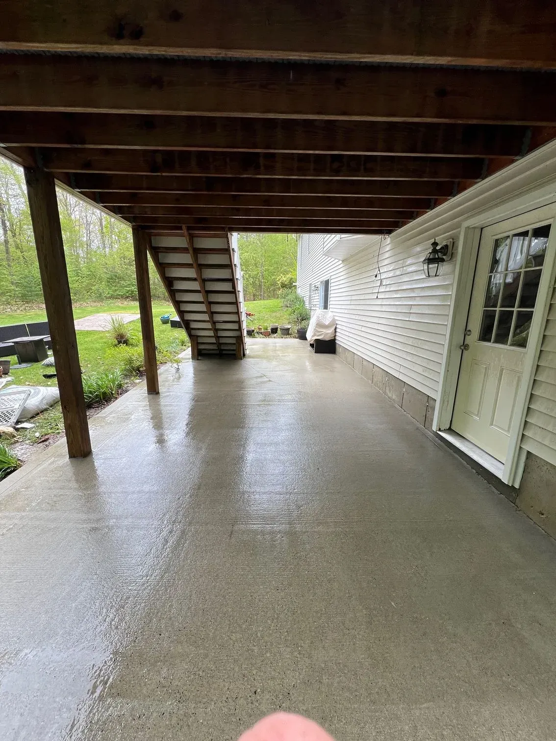 A person is standing in front of a house with a covered porch and stairs.