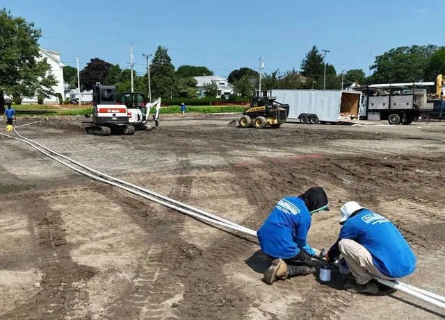 Two construction workers are working in a dirt field.