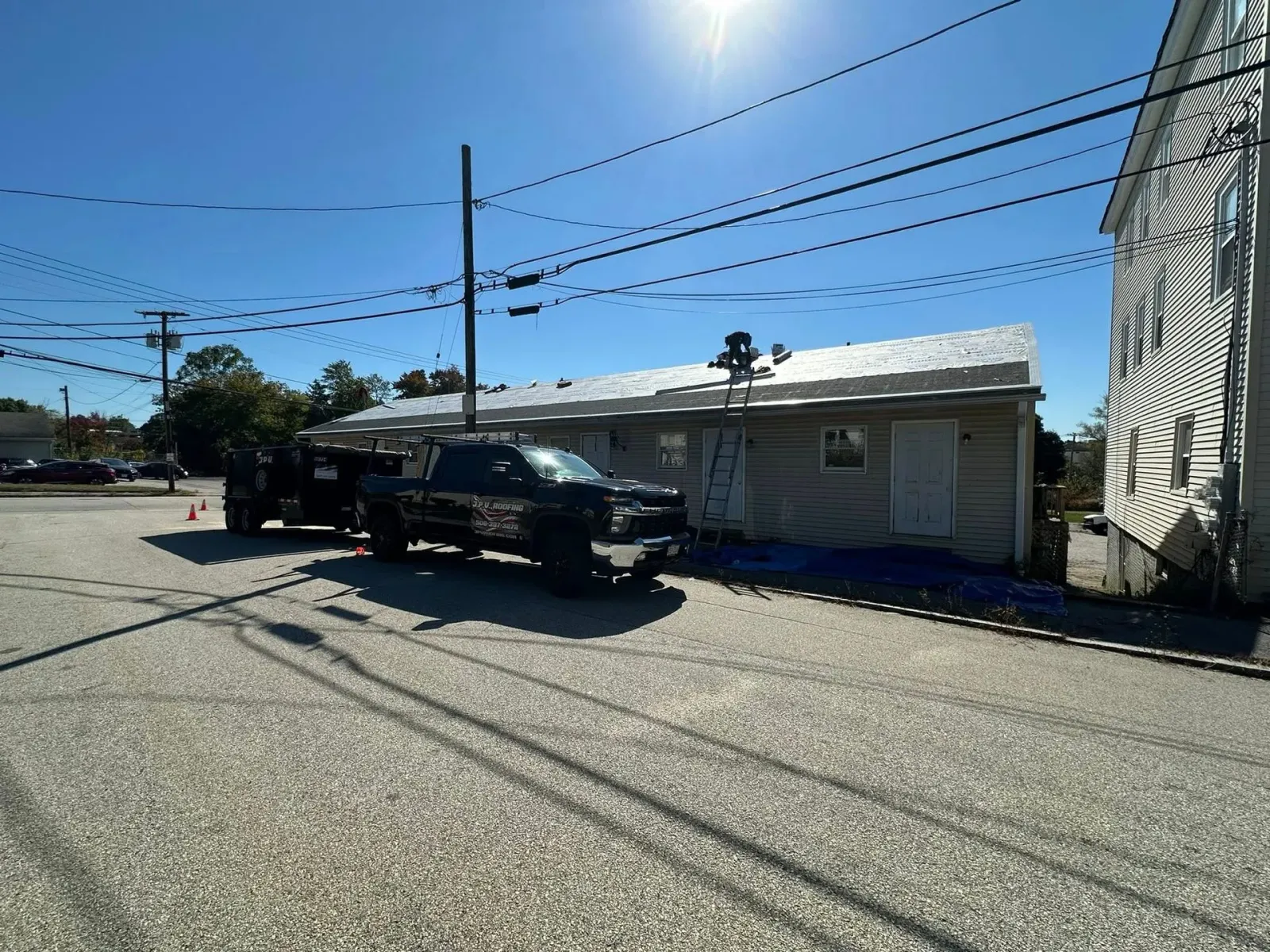 Truck with trailer parked near a building where roof work is in progress on a sunny day.
