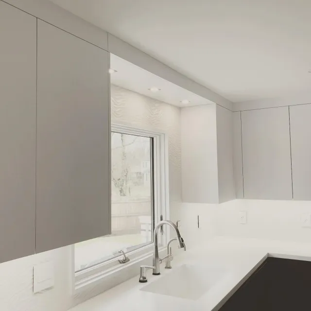 Modern kitchen interior with gray cabinets, a large window, and a white countertop featuring a built-in sink and faucet. Recessed lighting illuminates the space.