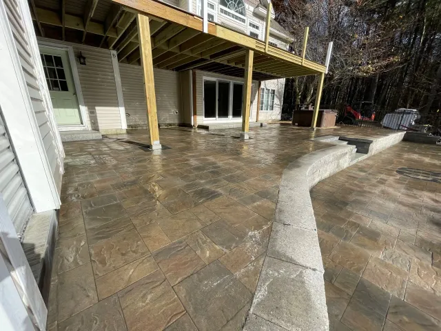 A large patio with a wooden deck and stairs in front of a house.