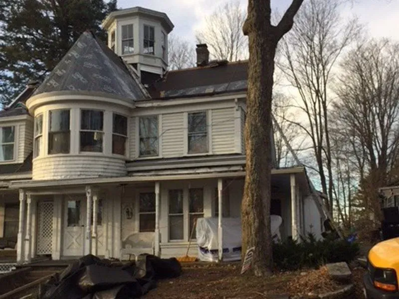 Victorian-style gray house with turret, front porch, and bare trees in the yard