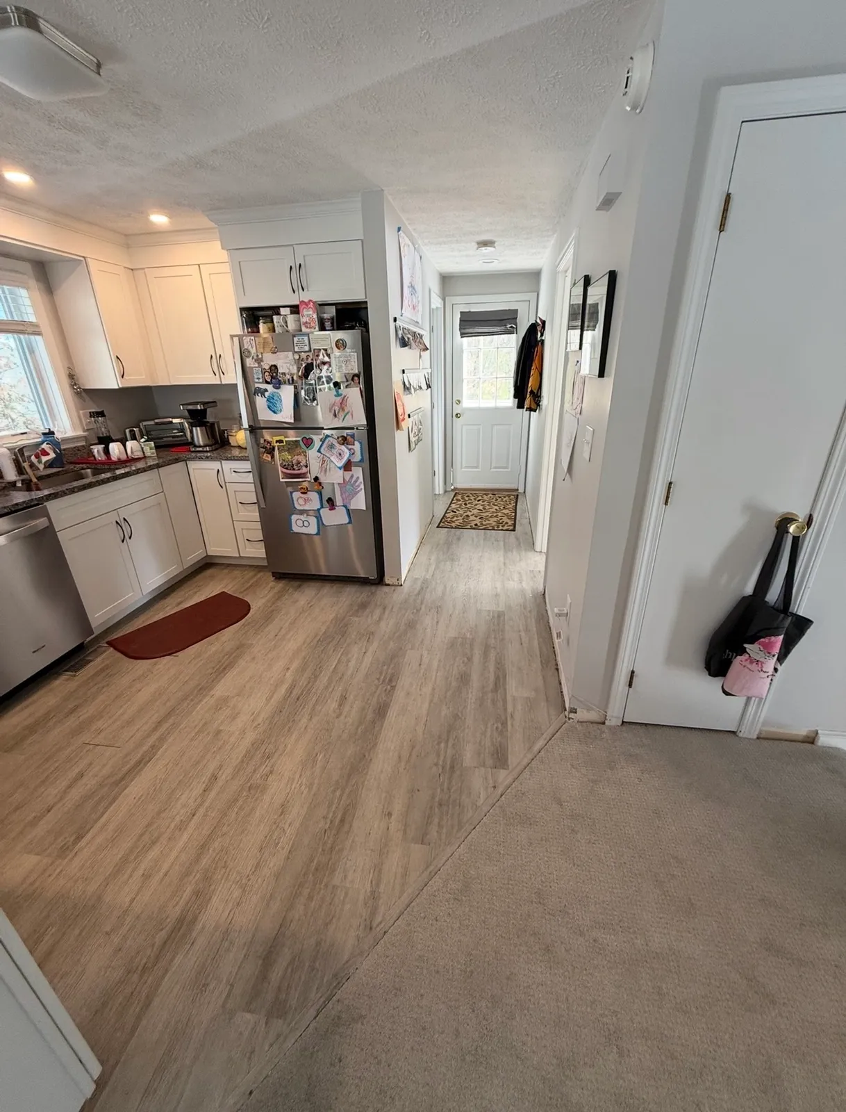 White shaker kitchen with stainless appliances and new wood-look LVP flooring transitioning to hallway