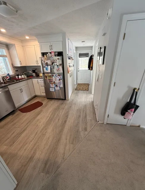 White shaker kitchen with stainless appliances and new wood-look LVP flooring transitioning to hallway