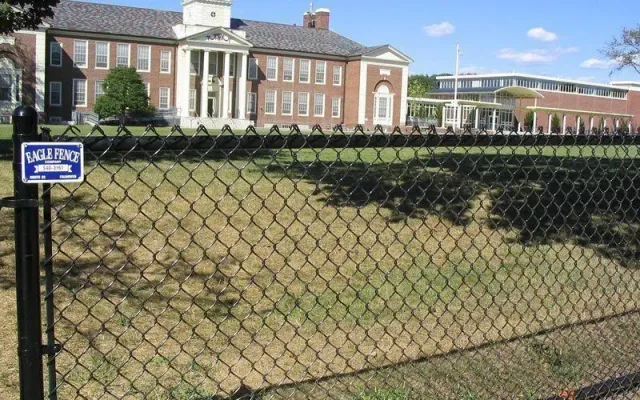 A black chain-link fence with an Eagle Fence sign stands in front of a brick building with white pillars on a sunny day.