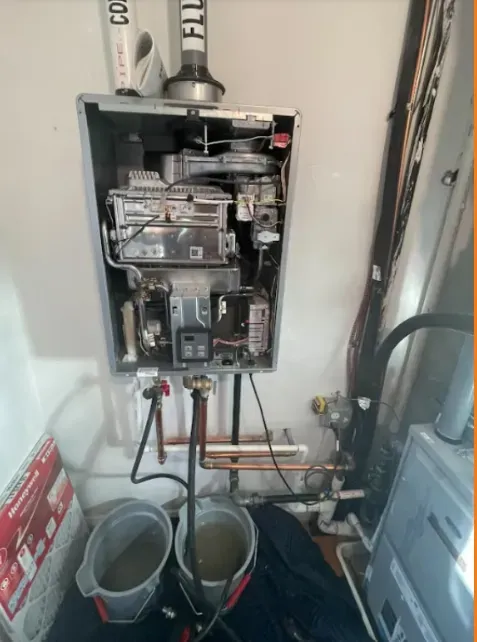 Open electrical breaker panel in utility closet with copper piping and buckets below