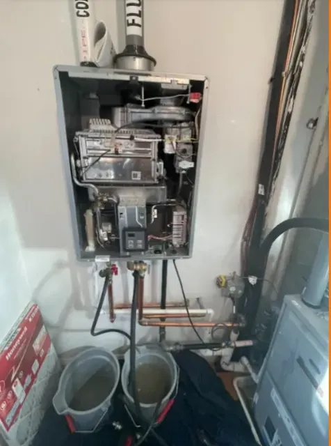 Open electrical breaker panel in utility closet with copper piping and buckets below