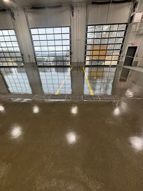 Inside a building with open garage doors. The floor is wet and reflects the bright lights overhead.