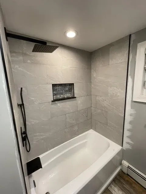 Bathroom shower with gray tiled walls, a built-in niche, a rainfall showerhead, and a handheld shower. Small window and a ceiling light.