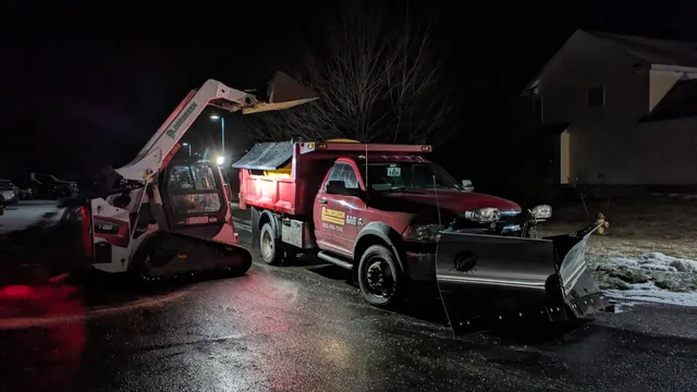 Globe Green plow truck and track loader on a commercial lot during a winter storm in Concord, NH