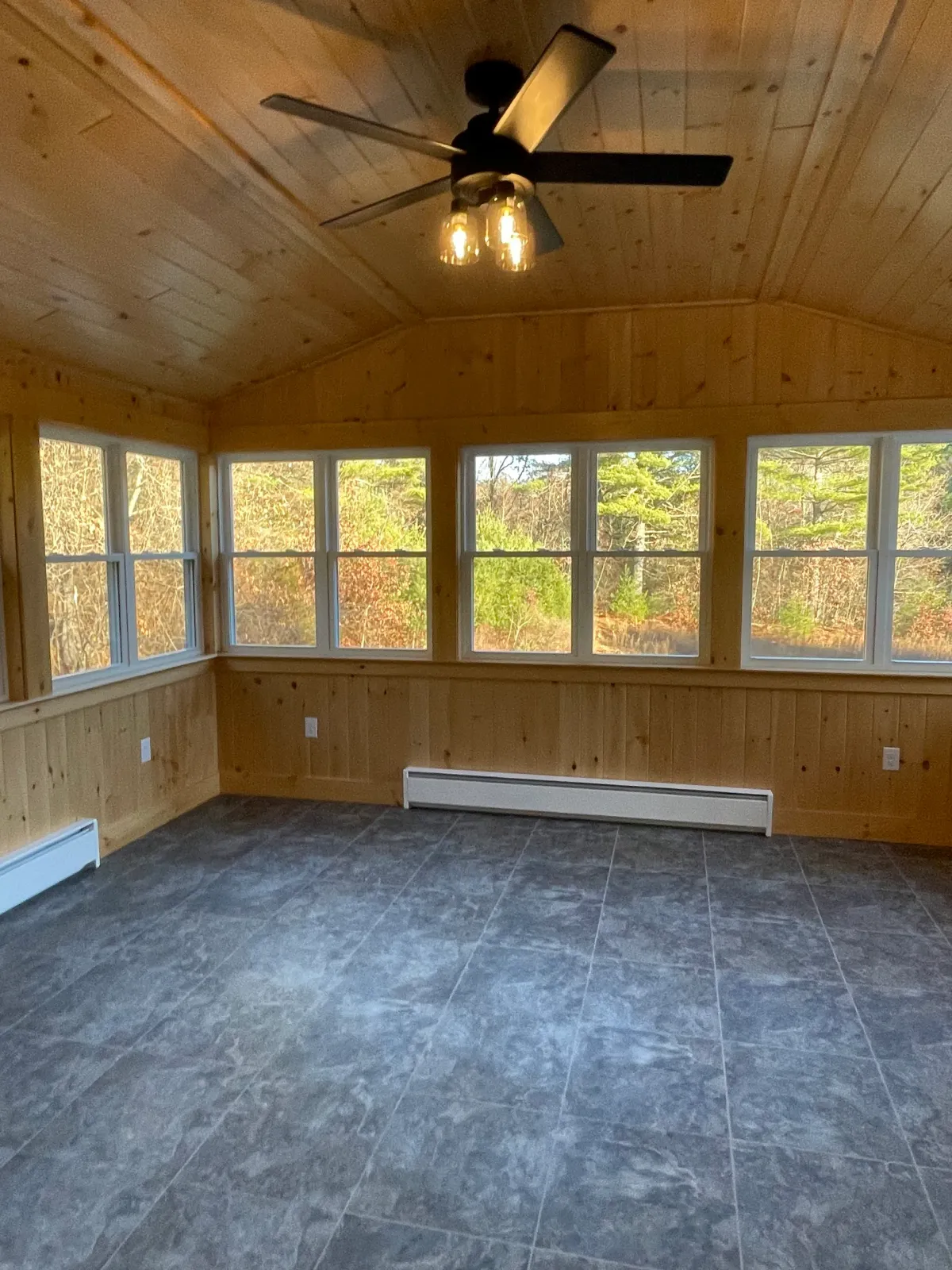 An empty room with a ceiling fan and lots of windows