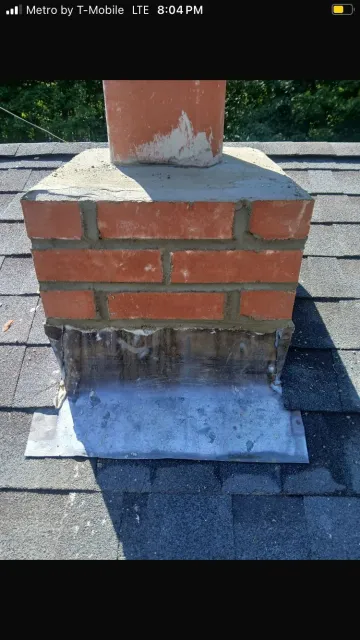Brick chimney on a shingled roof with a metal flashing base and a clay flue.