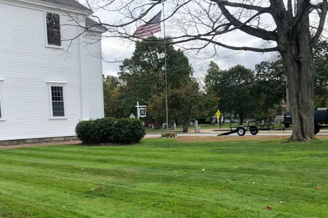 White building with cross, American flag, trees, and grass