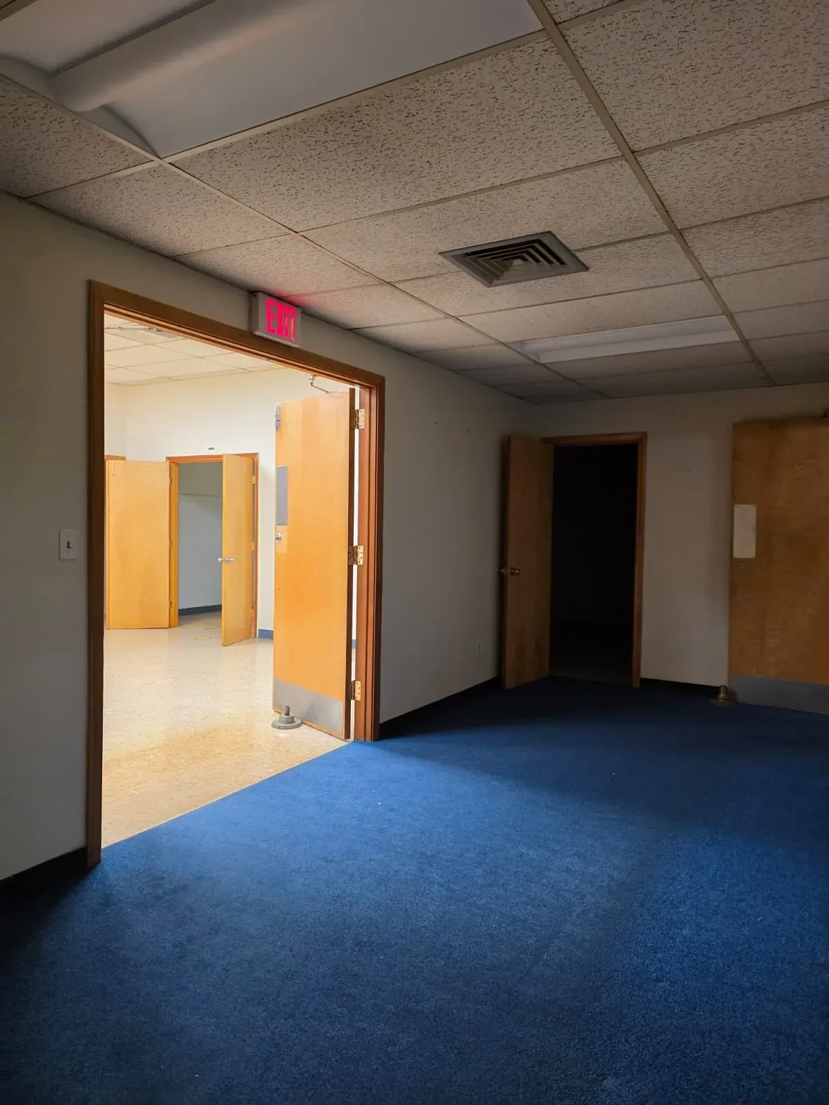 Empty hallway with blue carpet, open doorway to a lit room, and a dark doorway on the right.