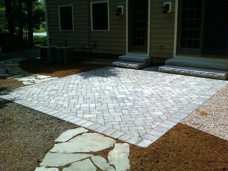 Stone patio and gravel courtyard beside a house with a paved walkway and steps.