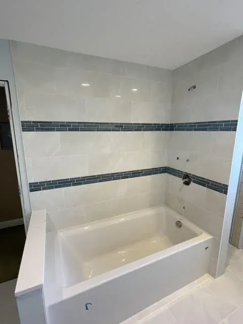 Bathroom with white bathtub, tiled walls with horizontal blue and gray decorative tiles, and plumbing fixtures.