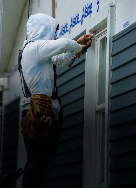 Construction worker installing window trim on a blue siding house.