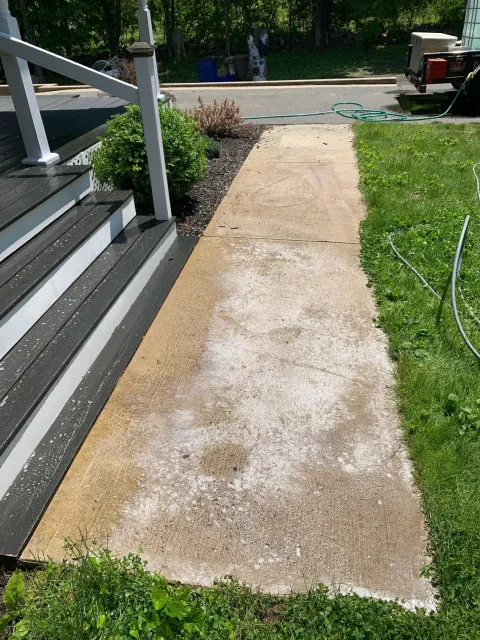A concrete walkway next to a house with stairs and grass.