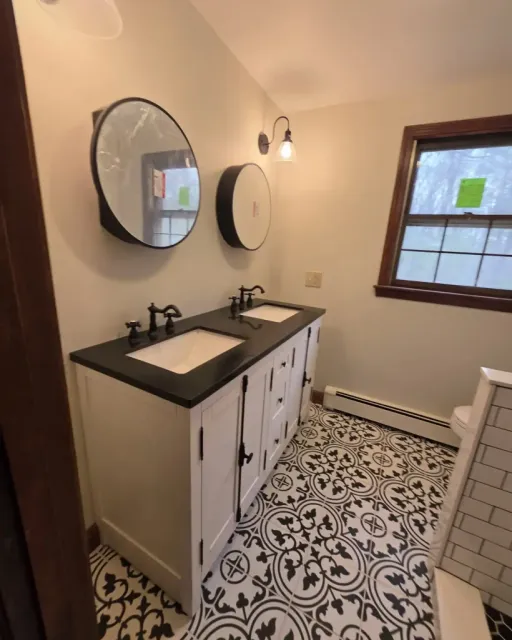 A bathroom with a double vanity, black countertop, circular mirrors, and bold black-and-white patterned floor tile.