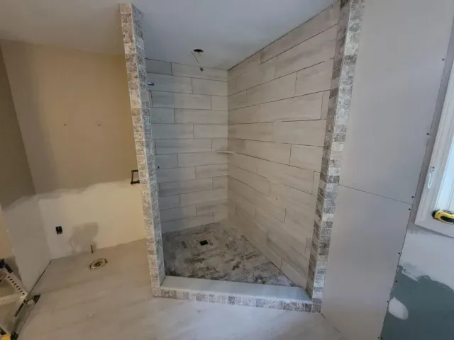 Bathroom under renovation with tiled shower stall and unfinished drywall around it