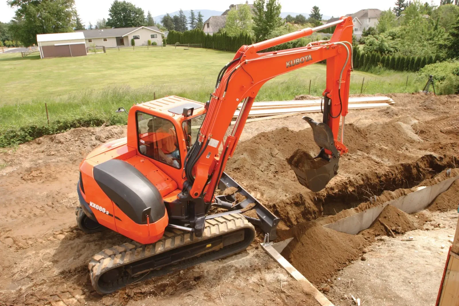 Orange excavator digging a trench in a dirt field near a house