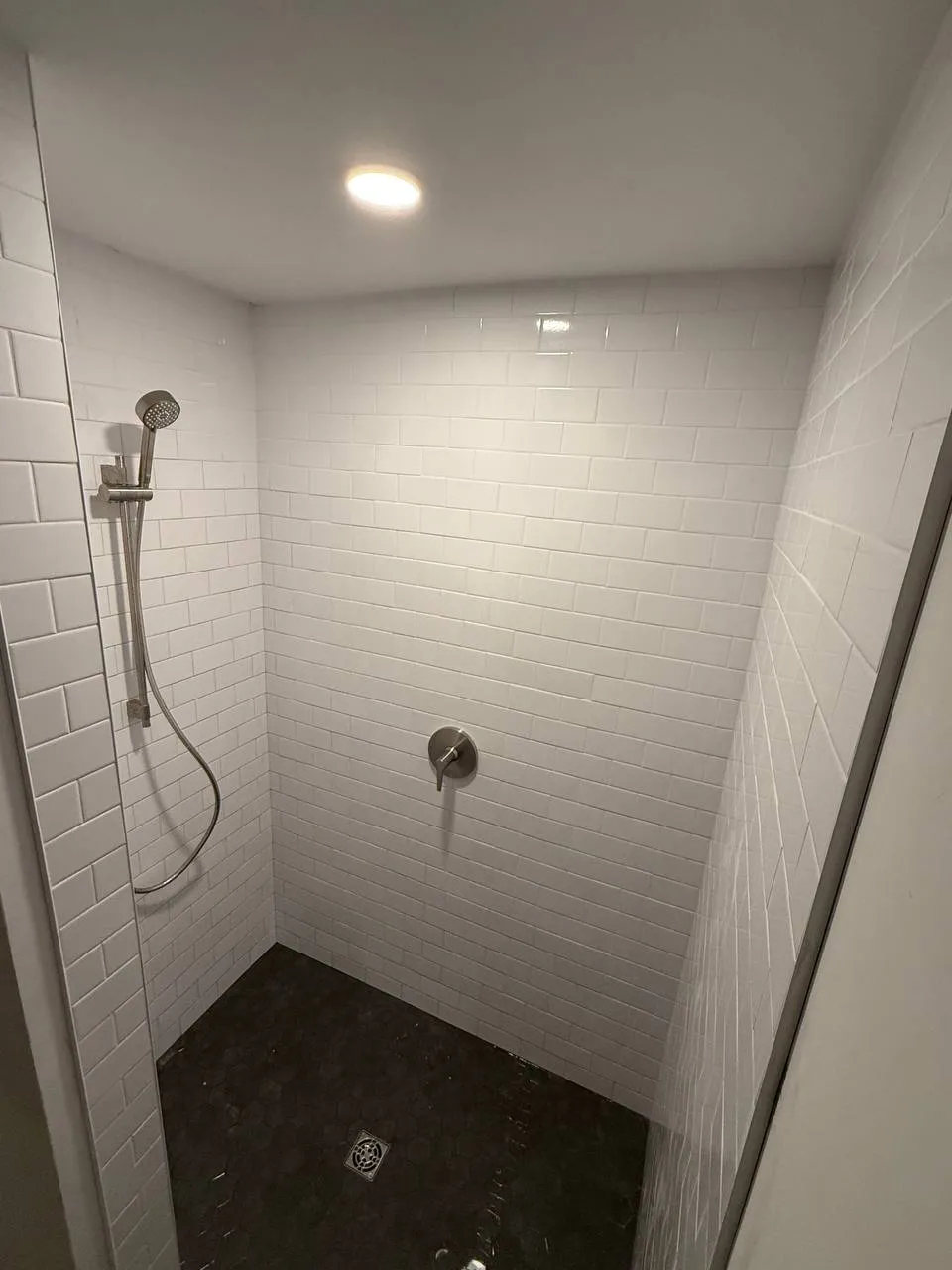 Tiled walk-in shower with handheld sprayer on slide bar and hex mosaic floor