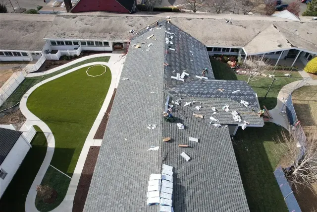 Aerial view of a damaged gray roof beside a curving white walkway and green lawn.