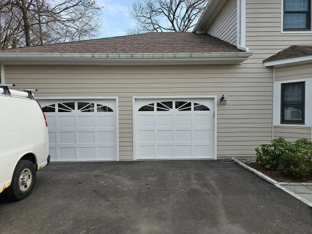 Two-car garage with white doors beside a beige house, with a white van parked on the left.