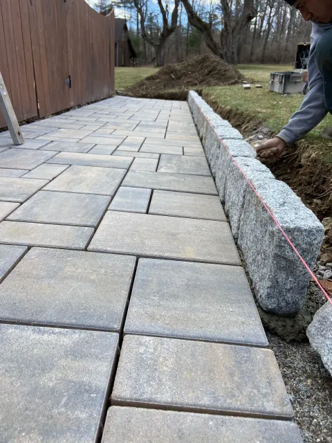 Person laying gray pavers for a patio, with a retaining wall being built.