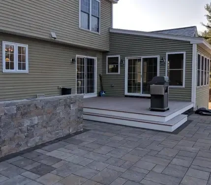 Exterior photo of home with new stone patio, outdoor kitchen, and deck addition