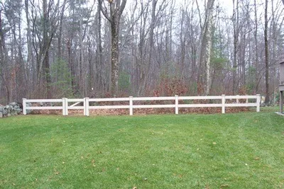 White post-and-rail fence at a wooded property line