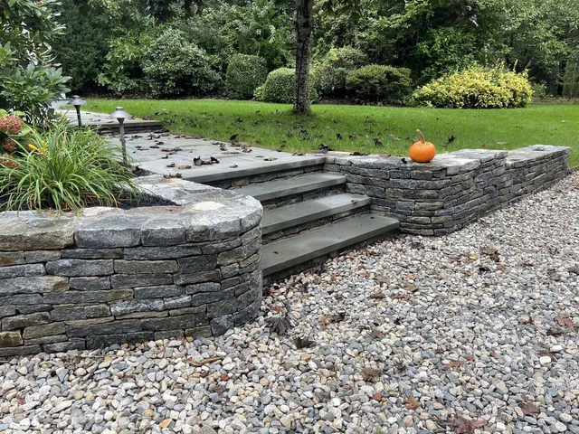 Bluestone steps set between drystack stone retaining walls, river-rock drainage at base, autumn pumpkin on the cap stone