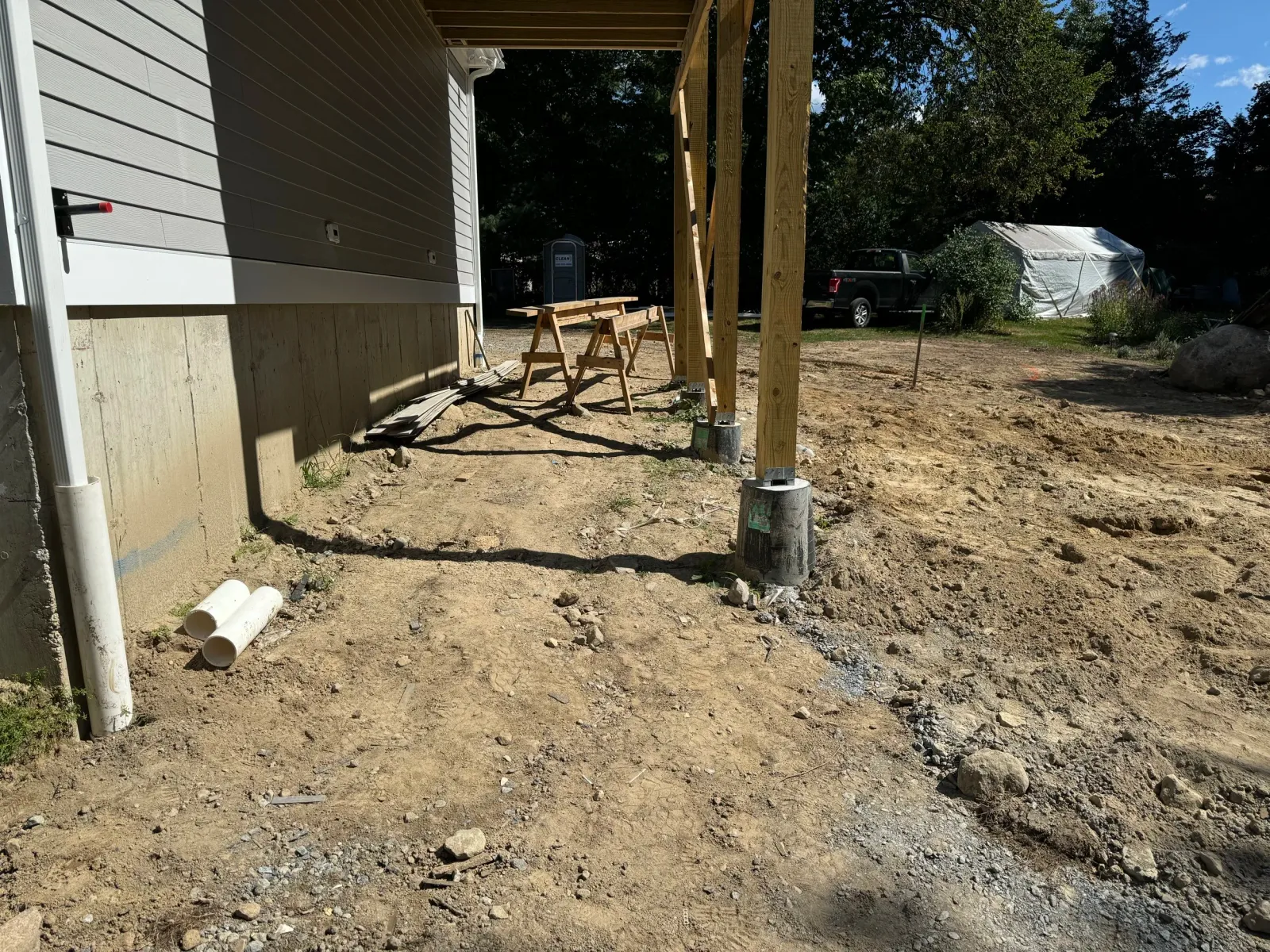 Construction site with wood framing, concrete foundation, pipes, and parked truck.