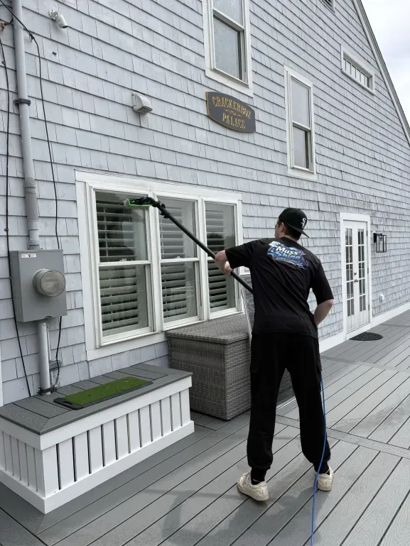 Mass Shine crew member cleaning first floor window with water-fed pole on shingle home South Shore Massachusetts