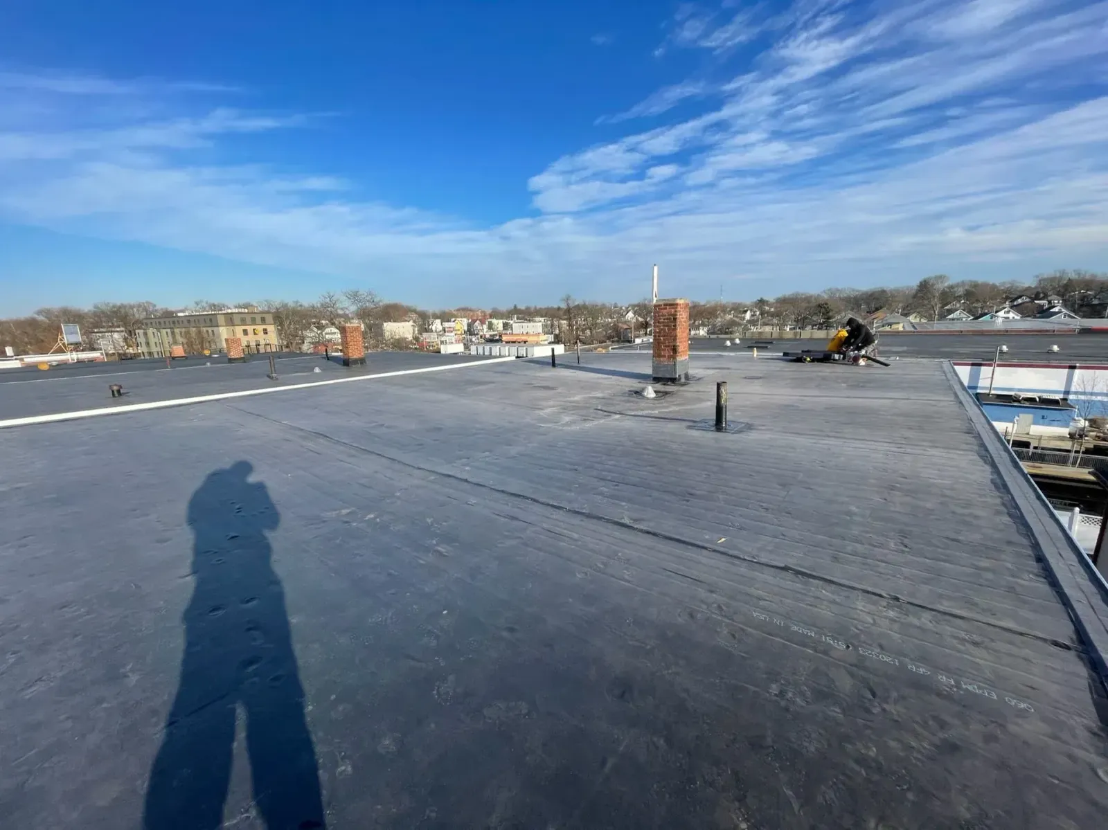 Flat, dark rooftop with a clear, blue sky. A person works in the distance.