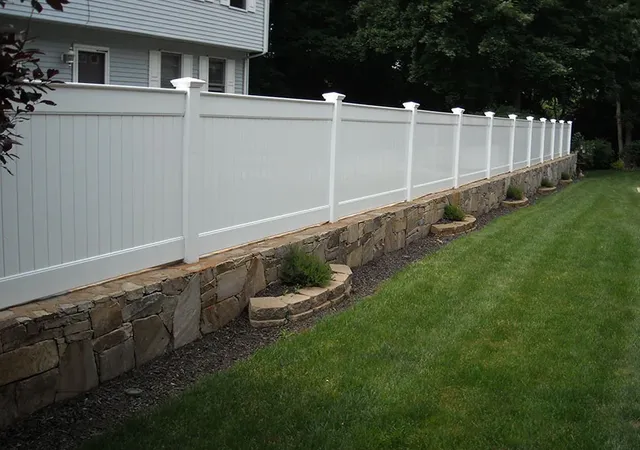 White vinyl privacy fence atop a stone retaining wall